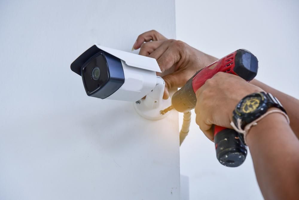A Person is Installing a Security Camera on a Wall With a Drill — River City Communications In Melinga, NSW