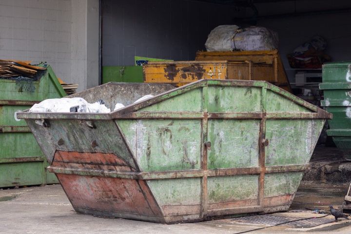 Green and rusted metal dumpster in an industrial garage, with debris piled inside