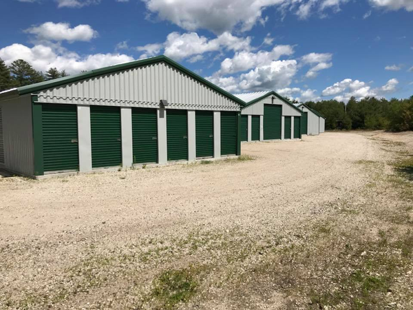 A row of storage units with green doors on a gravel road.