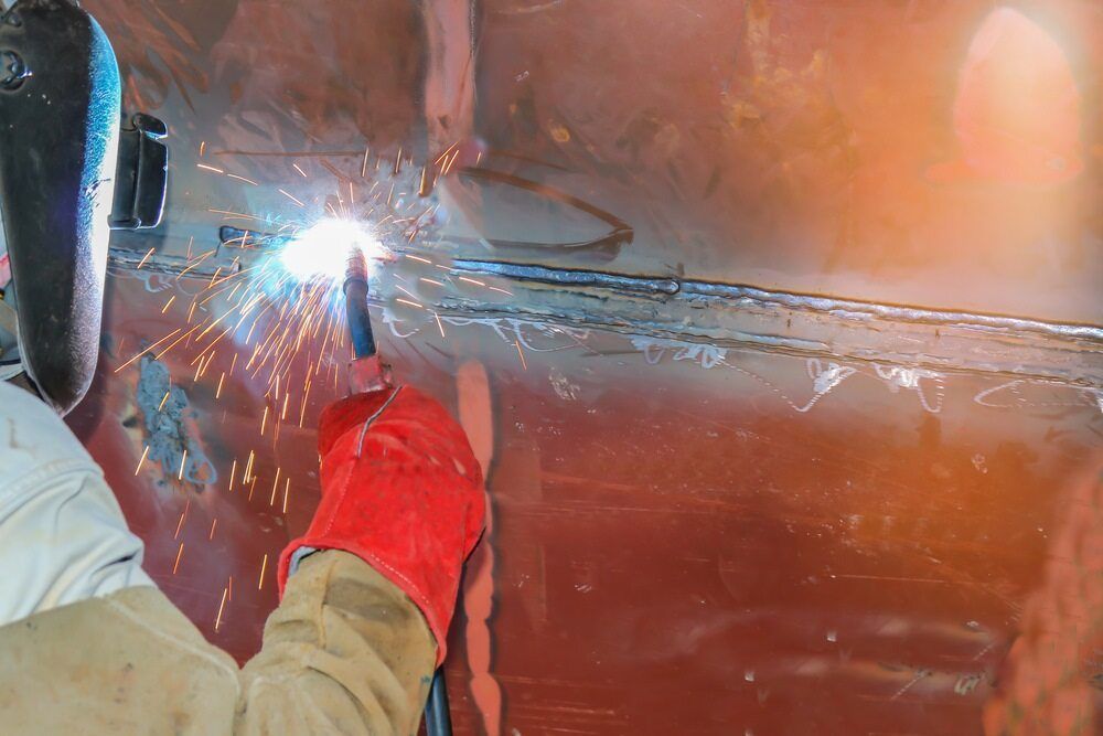 Man Welding the Side of a Metal Boat — Wright's Welding Operations In Ryan, QLD