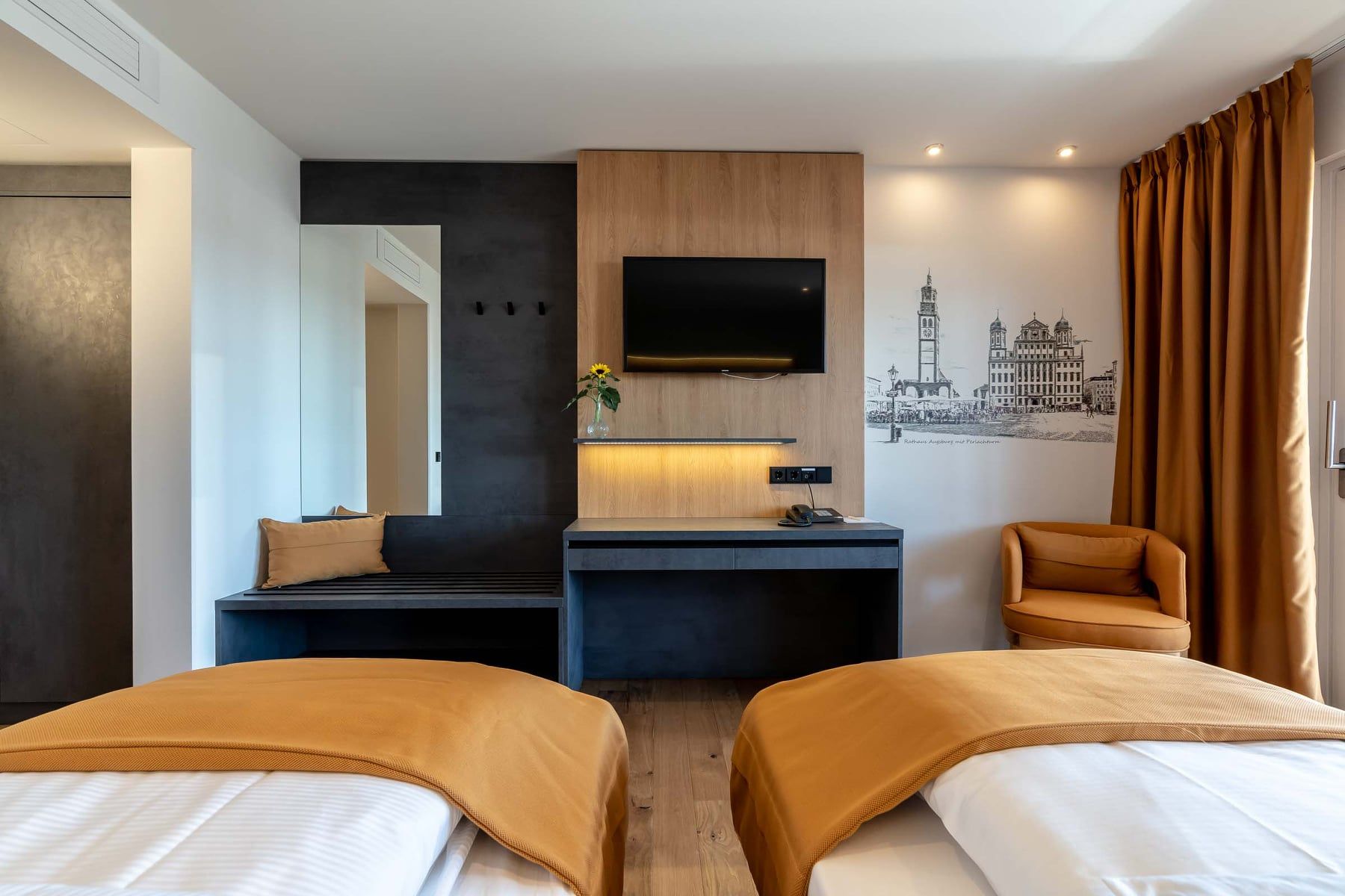 Twee eenpersoonsbedden met oranje dekens in een hotelkamer. Een bureau en een tv zijn zichtbaar.
