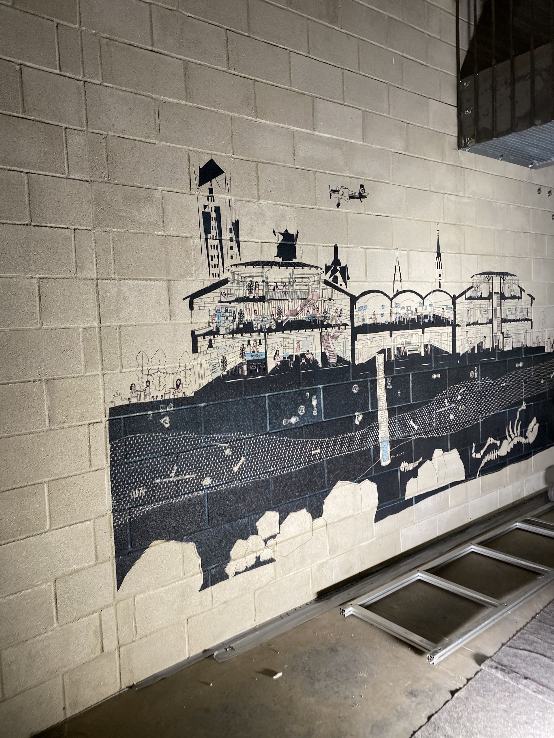 Zwart-wit muurschildering van een schip op een betonnen muur. Interieur, diverse ramen in de vloer.