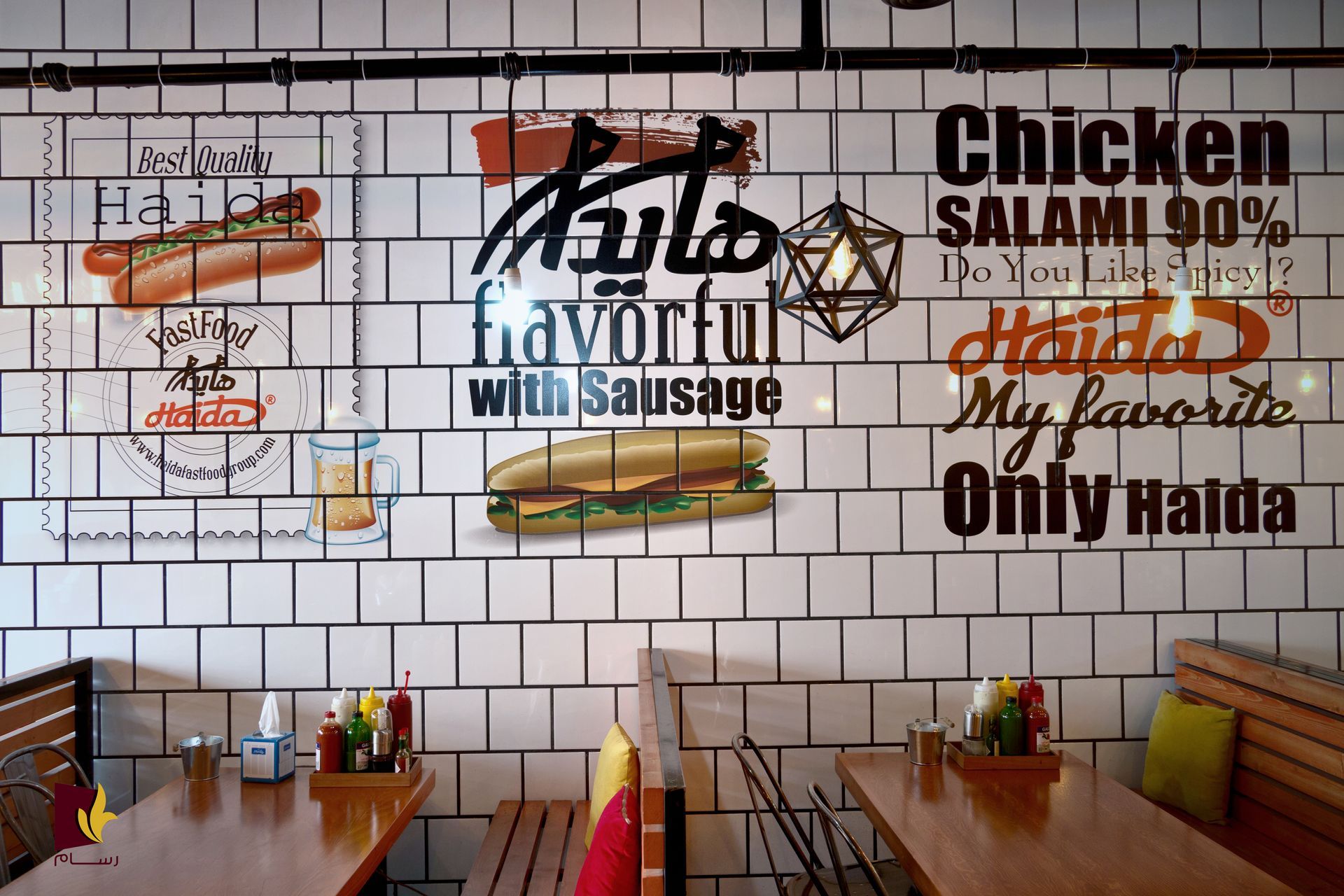 Interieur van restaurant met tegelmuurschilderingen waarop eten is afgebeeld, waaronder een hotdog en een sandwich, boven houten tafels.