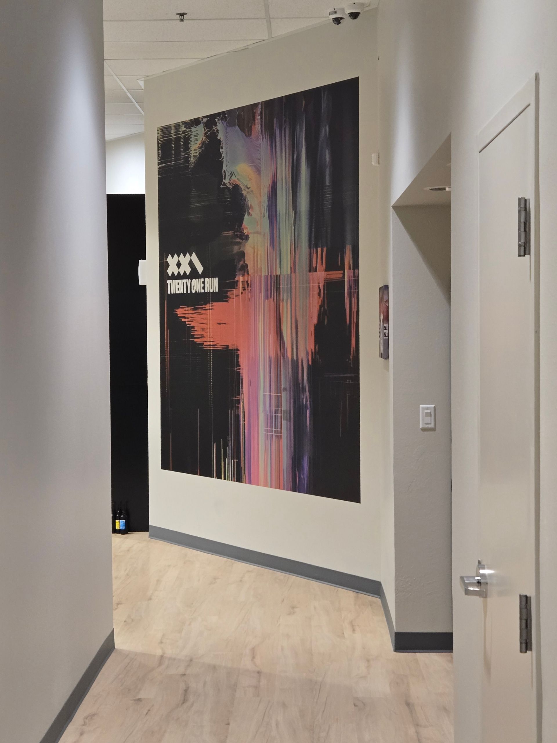 Hal met kleurrijk abstract kunstwerk aan de muur. Lichte houten vloeren en neutrale muren.
