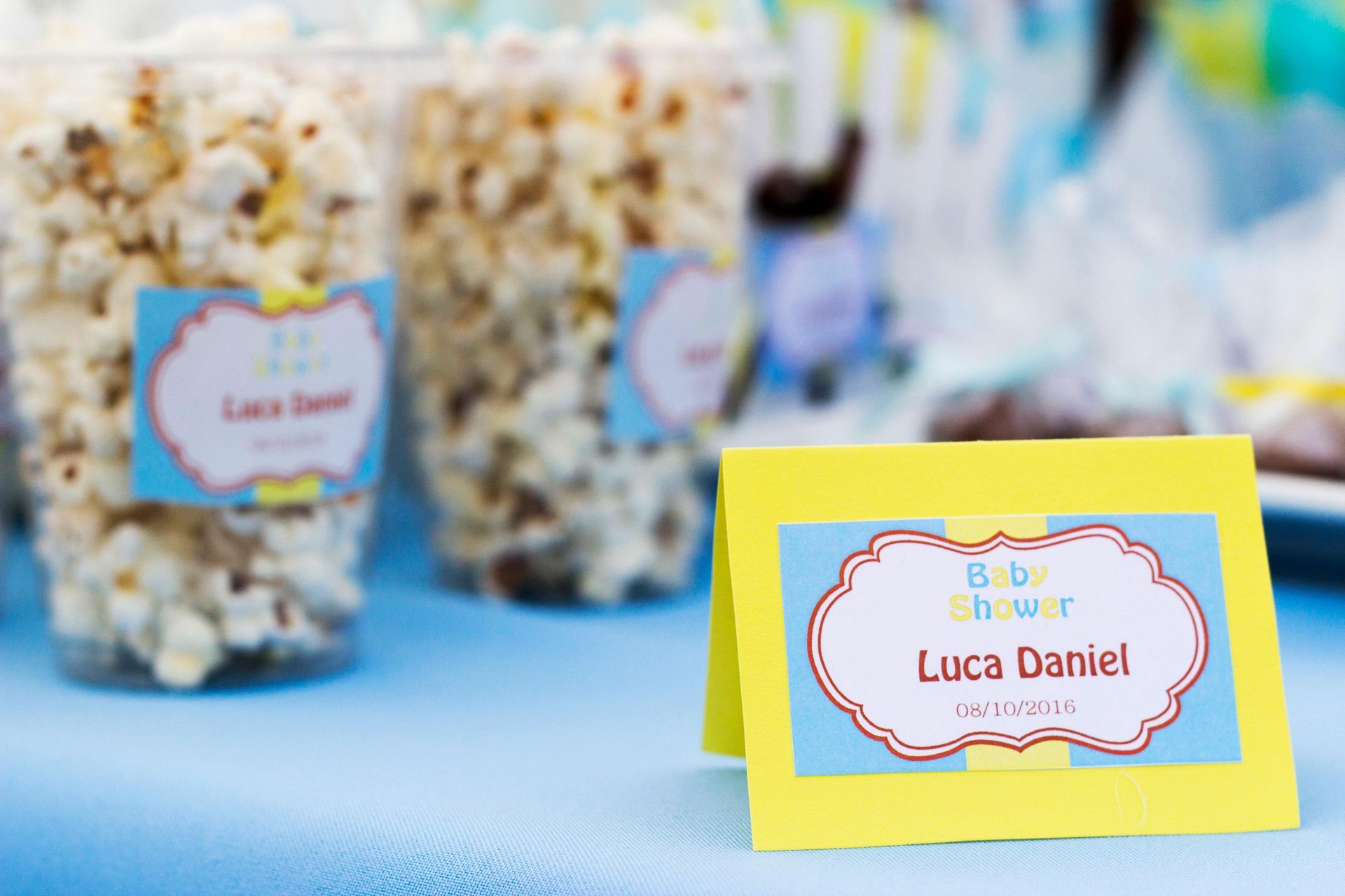 Baby shower with popcorn in clear cups and a yellow card with the name 