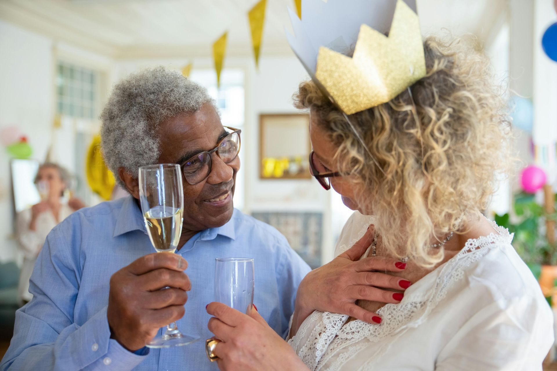 Man and woman with glasses, champagne flutes, celebrating, woman wearing gold crown, party setting.