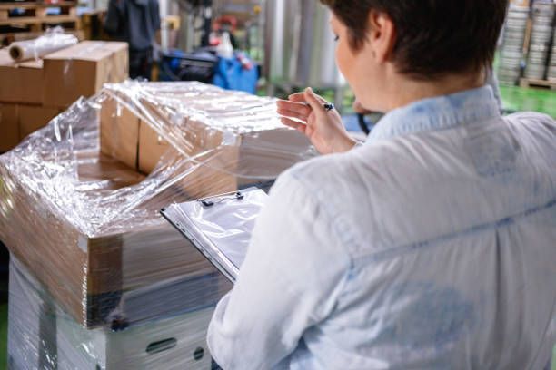 A woman is sitting at a table in a warehouse looking at a clipboard.