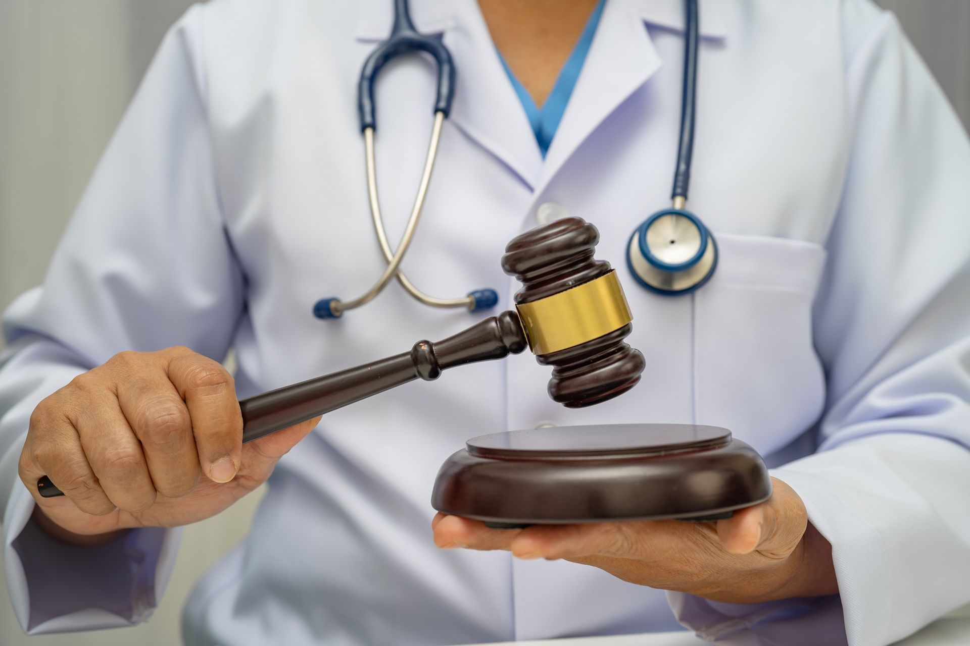A doctor with a stethoscope around his neck is holding a wooden gavel.