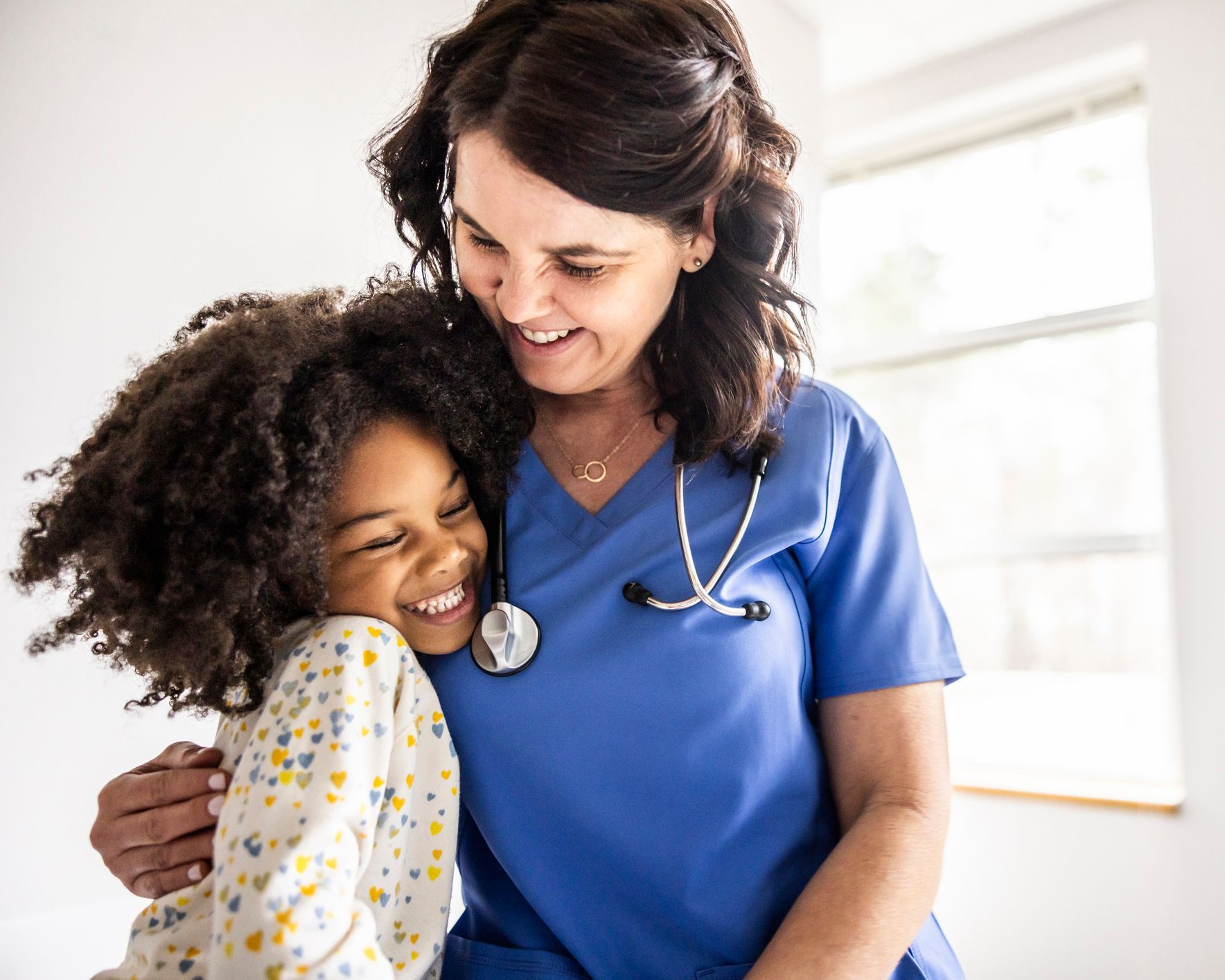 A nurse is hugging a little girl with a stethoscope around her neck.
