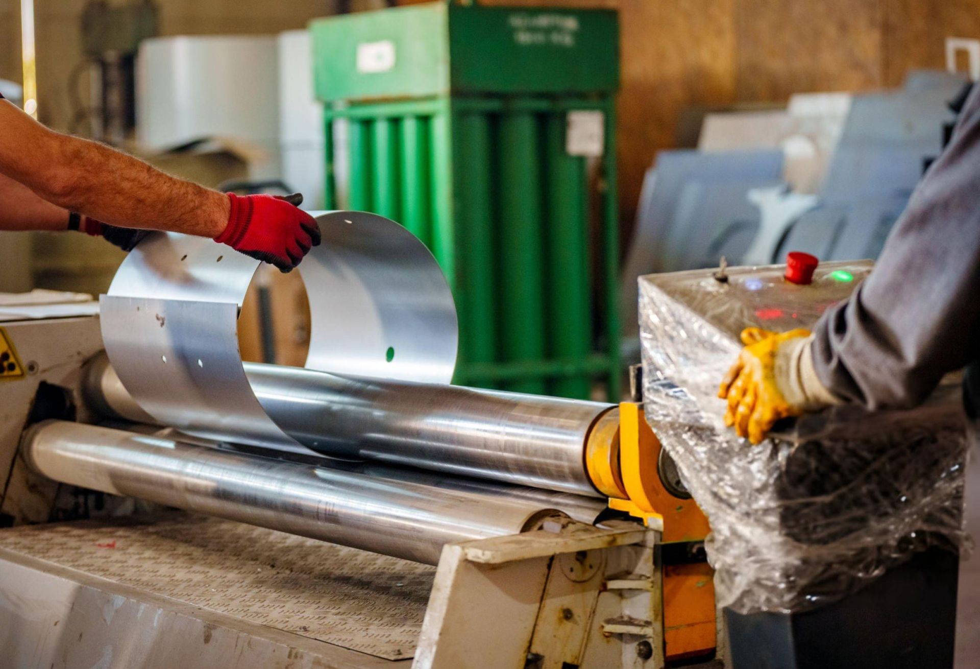 Worker feeding a flat sheet of metal into a rolling machine