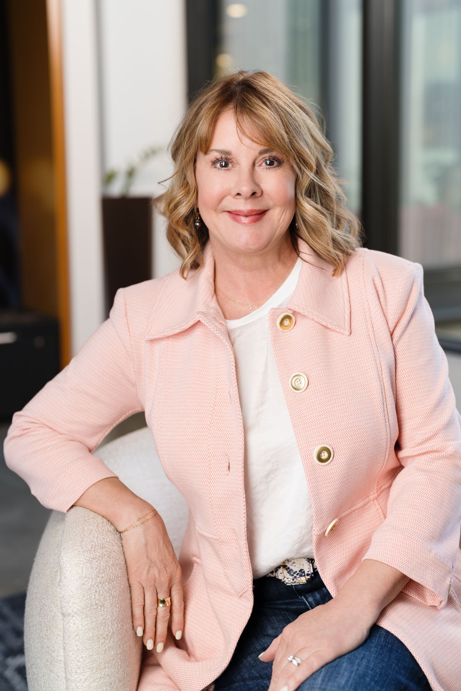 A woman in a pink jacket is sitting on a chair. Gayle Morris Real Estate | GUIDE Real Estate