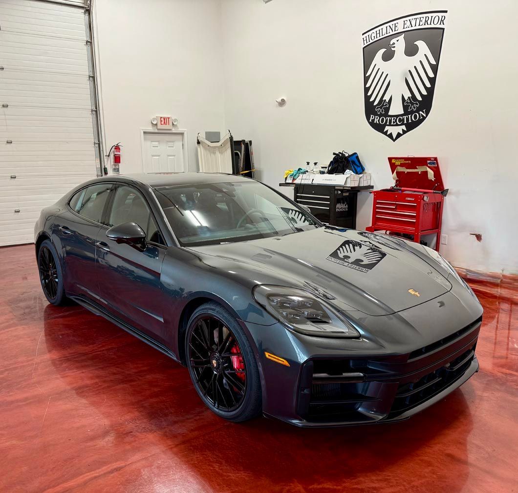 Dark gray Porsche Panamera in a garage with a red floor and a logo on the wall.