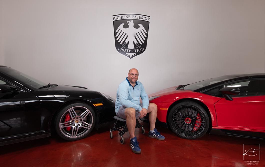 Man sitting between a black car and a red car in a showroom.