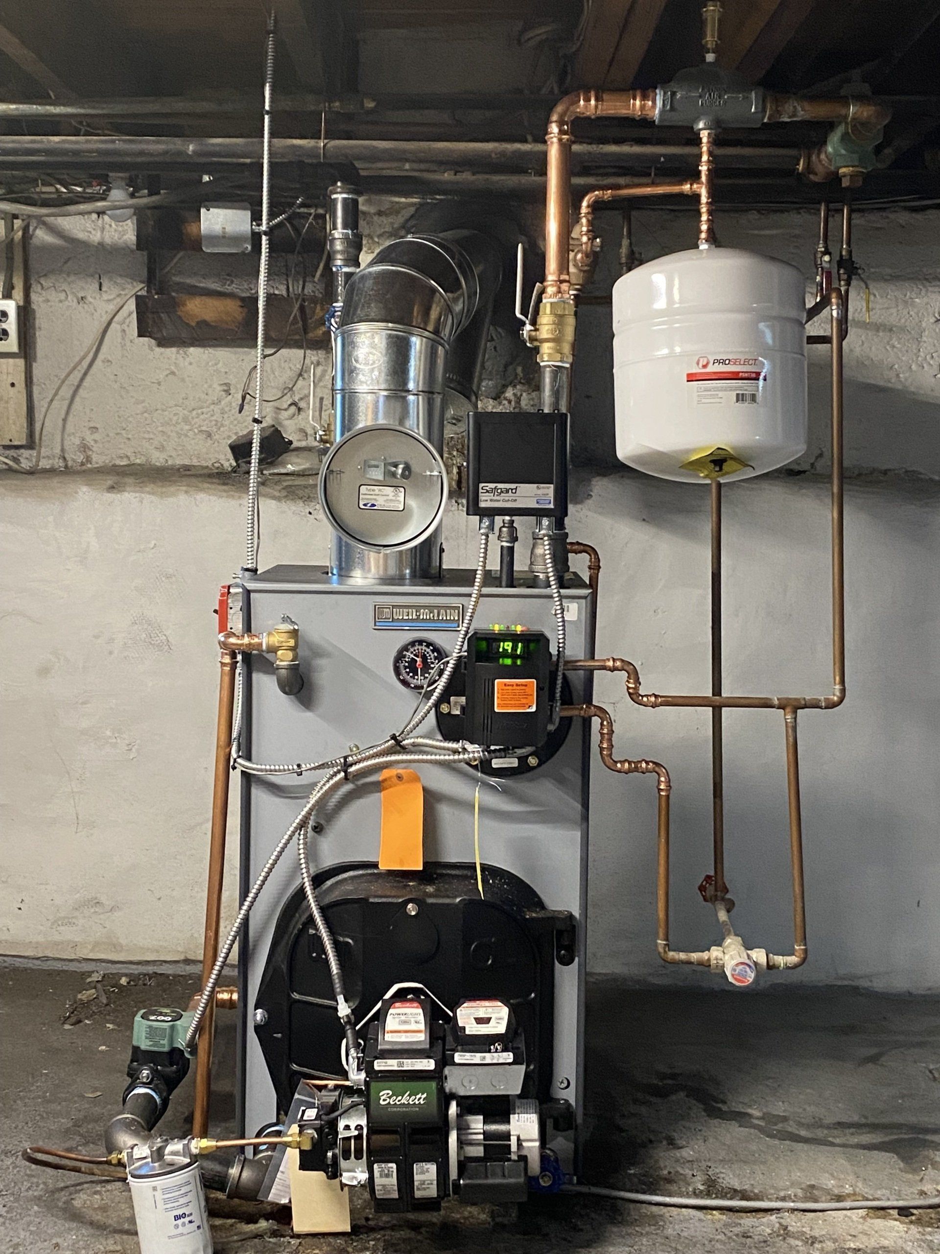 A boiler is sitting in a basement next to a water tank.