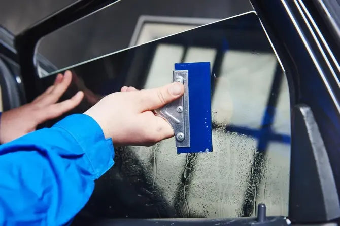 Hand using a blue squeegee to clear water from a car window