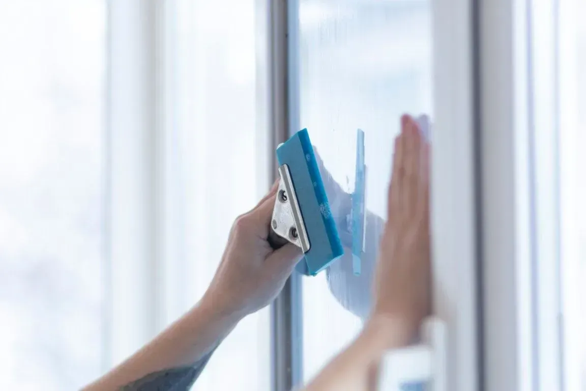 Hand cleaning a glass window with a blue squeegee and cloth