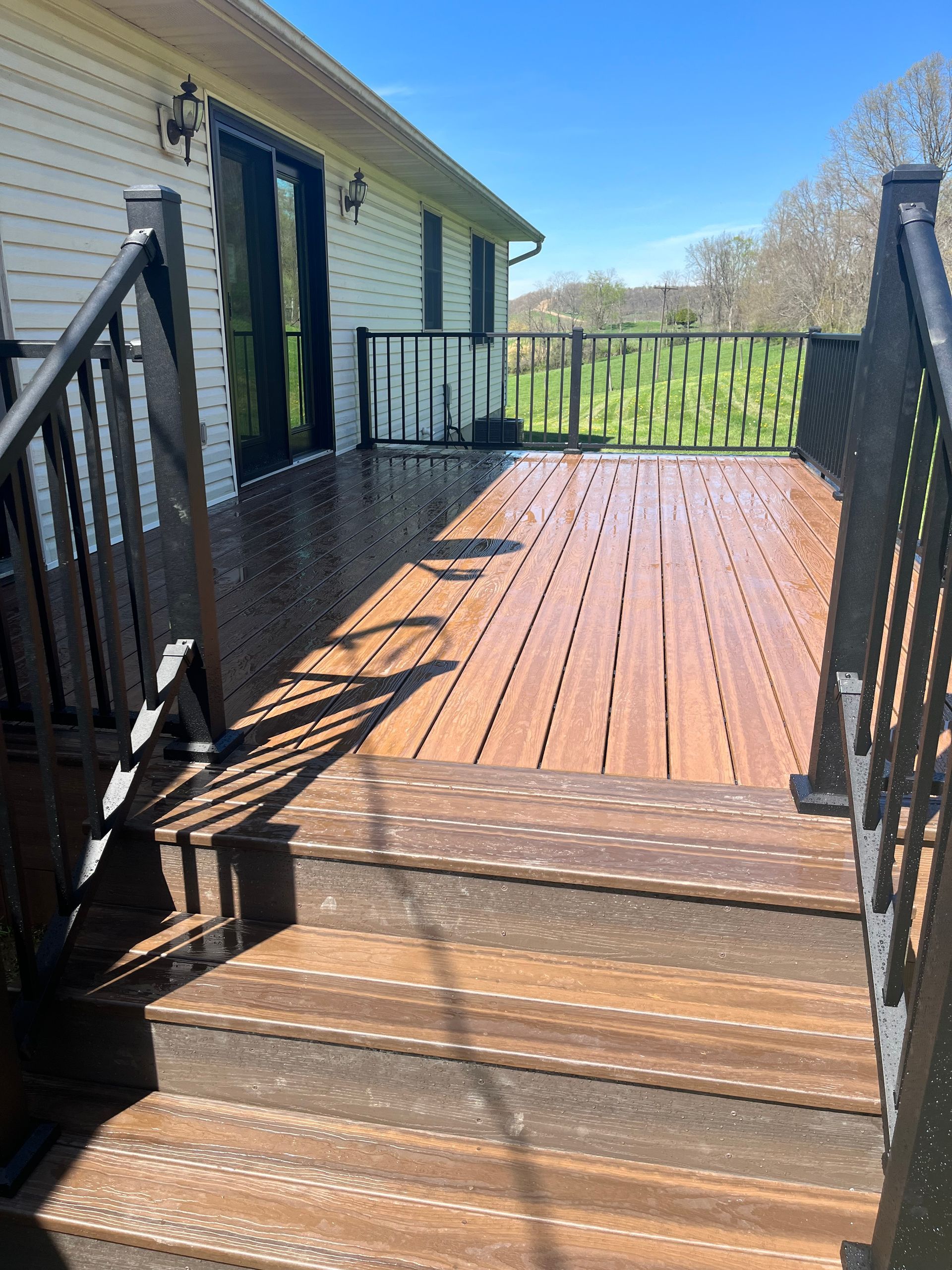 Composite deck with stairs, black railings, and a grassy field in the background on a sunny day.