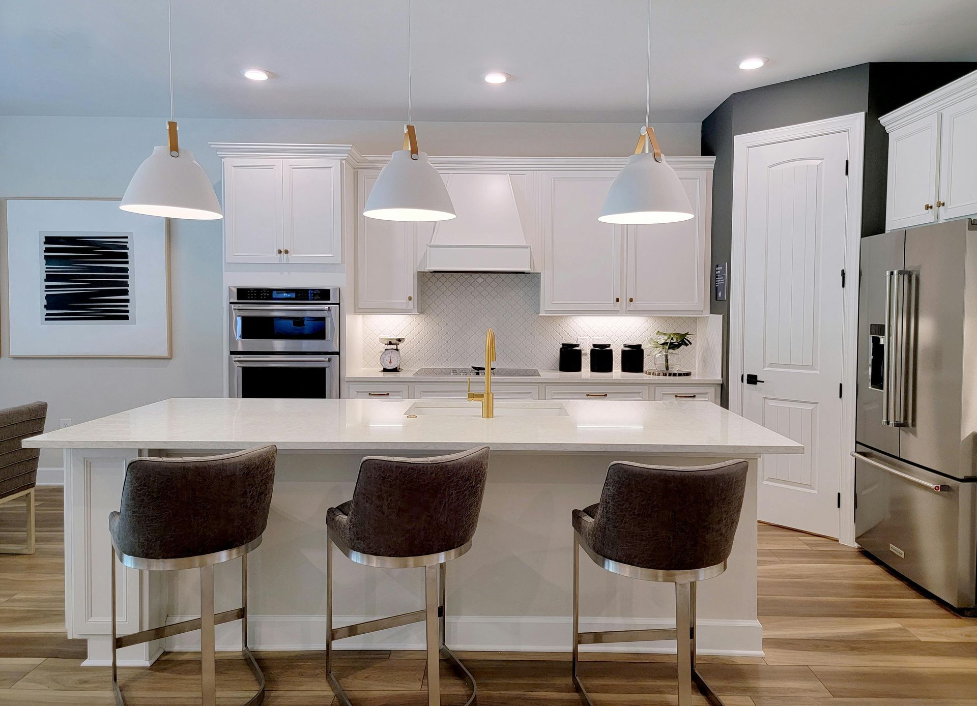 White kitchen with island, bar stools, pendant lights, stainless steel refrigerator.
