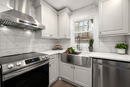 Bright white kitchen with stainless steel appliances, farm sink, and marble backsplash.