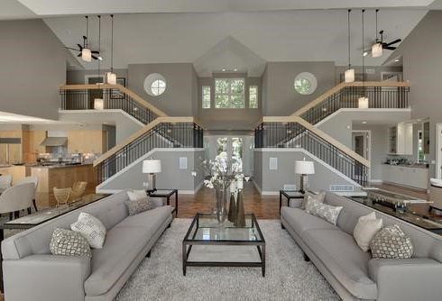 Spacious living room with two gray sofas, a glass coffee table, and a grand staircase.
