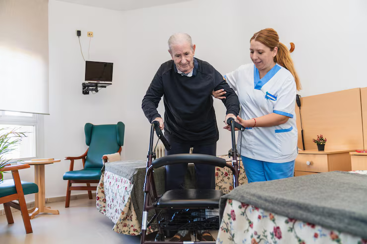 Caregiver assisting a person using a walker in a room; the person is walking.