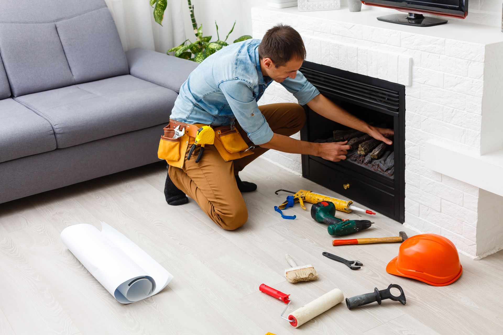 Man installing a black fireplace insert in a bright living room with tools on the floor.