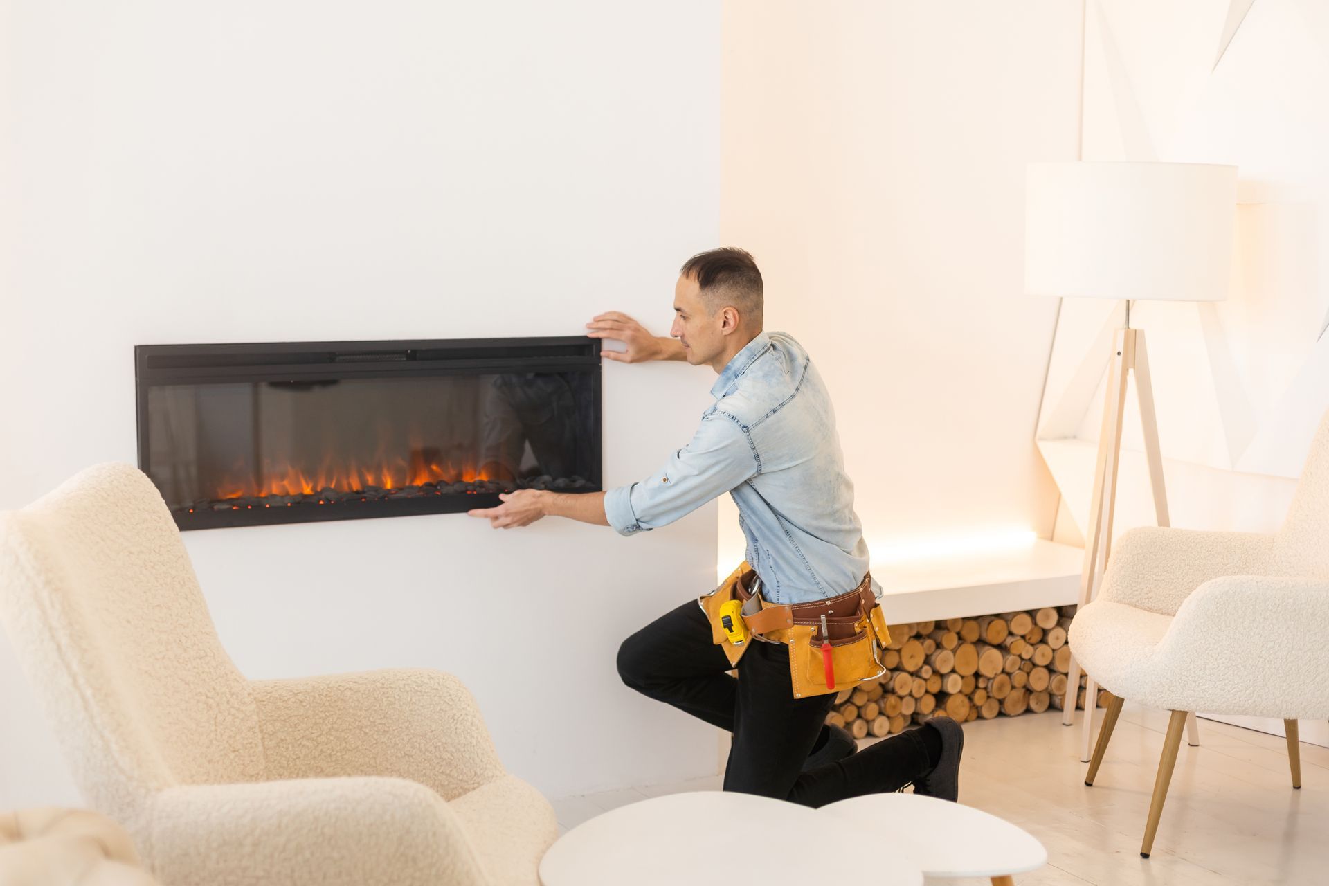 A fireplace worker installing an electric fireplace in an all-white room. A fireplace worker installing an electric fireplace in an all-white room.