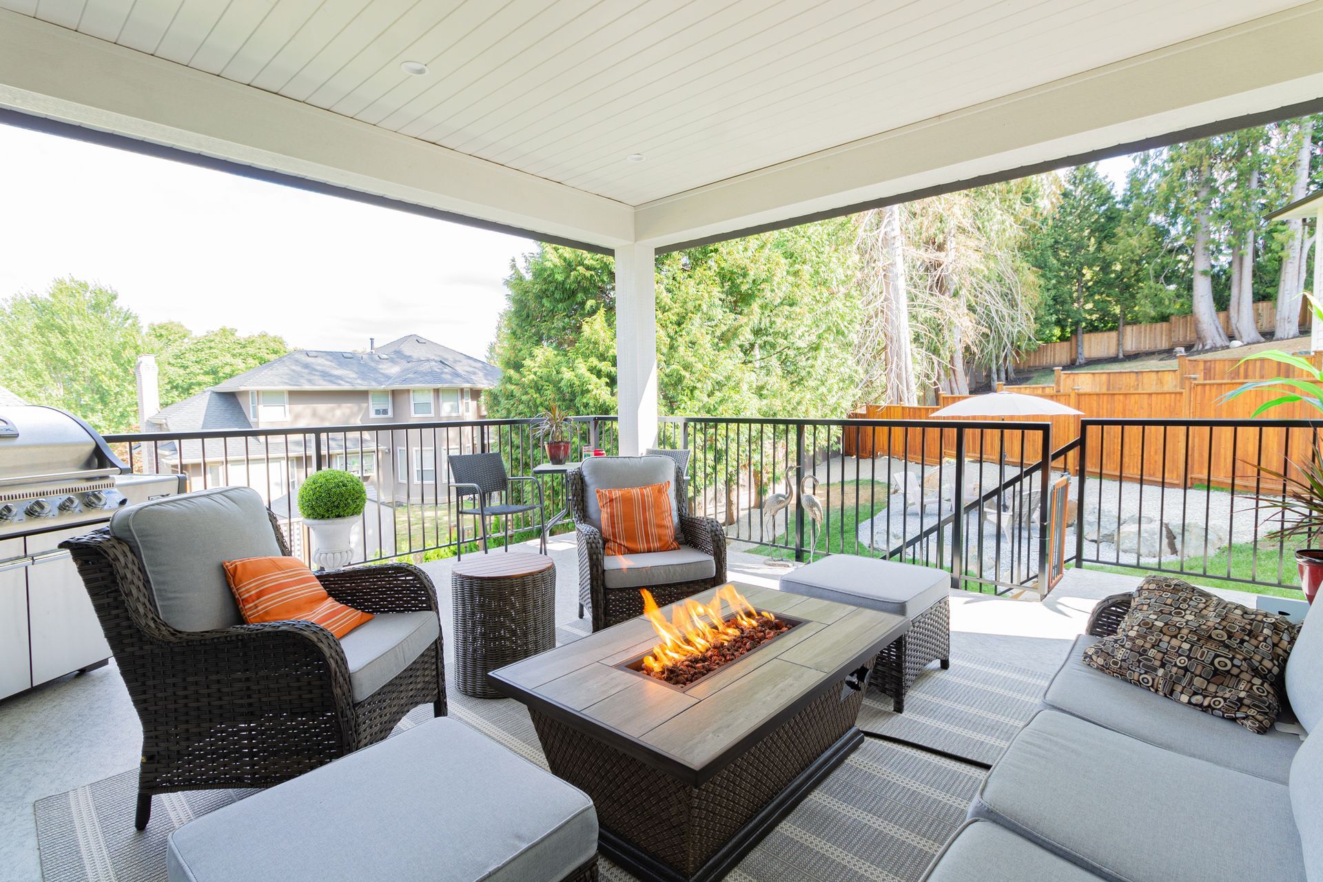 Covered patio with seating, fire pit, and view of a fenced backyard with greenery.