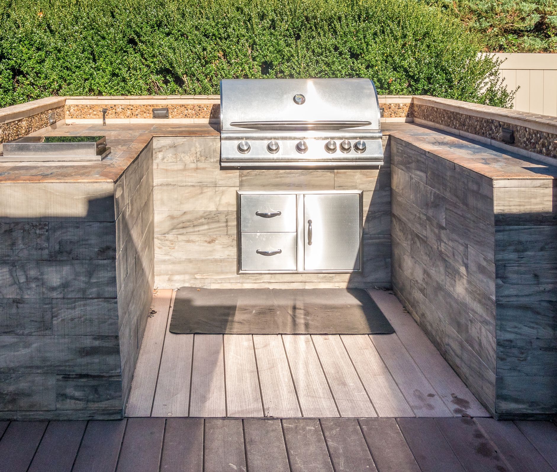 Outdoor built-in grilling area with stainless steel grill, cabinets, and concrete surround, on a wooden deck.