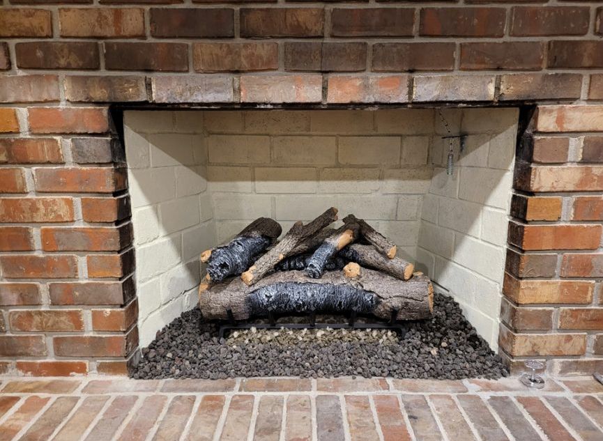 Brick fireplace with artificial logs, glowing embers, and a white interior.