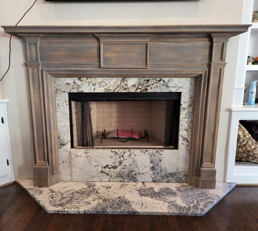 Fireplace with gray stained wood mantel and granite surround on dark wood floor.