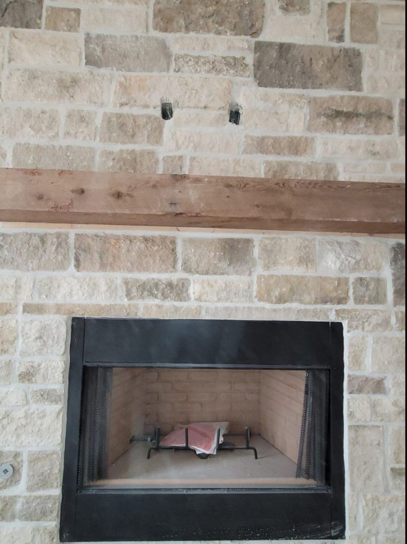 Stone fireplace with black surround, wooden beam, and recessed openings in stone wall.