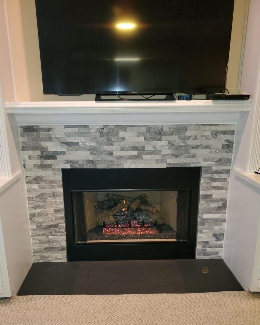 Fireplace with gray and white tile, black trim, and a lit fire, below a mounted TV.