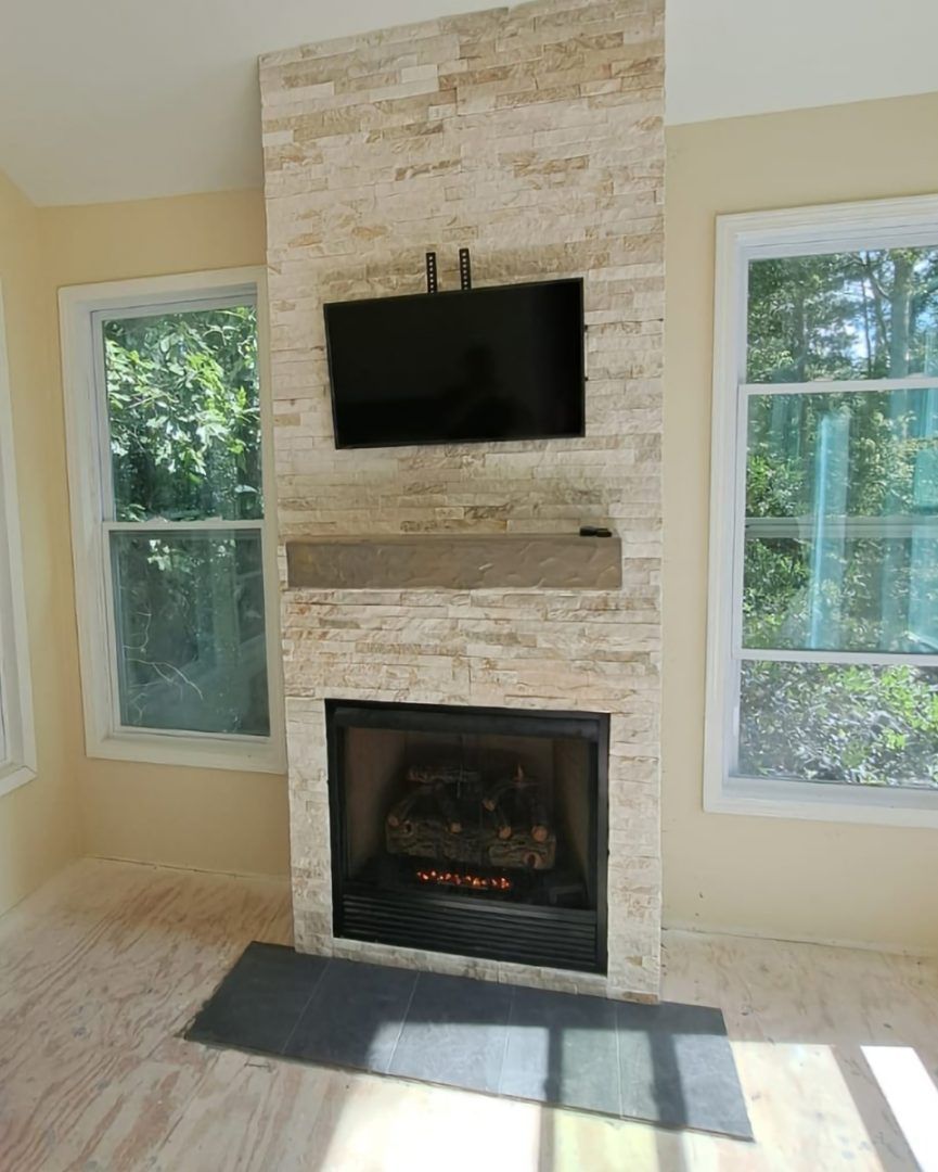 Fireplace with stone facade, TV, and mantel, flanked by windows. Beige walls, light wood floor.