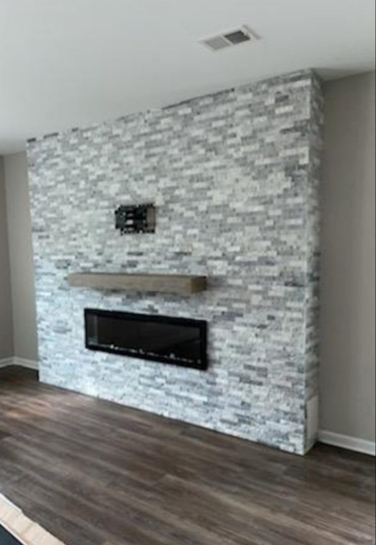 Fireplace with gray and white stone veneer wall, black electric insert, and wooden mantel.
