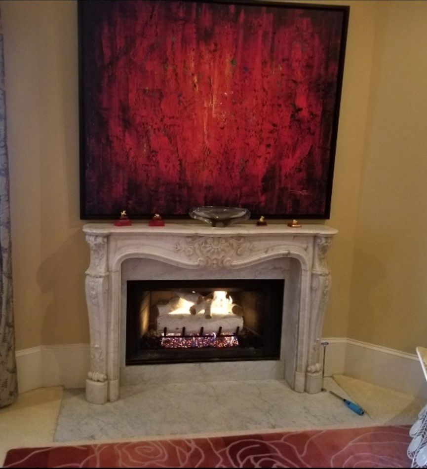 Fireplace with burning logs, topped by a red abstract painting. A few candles sit on the mantel.