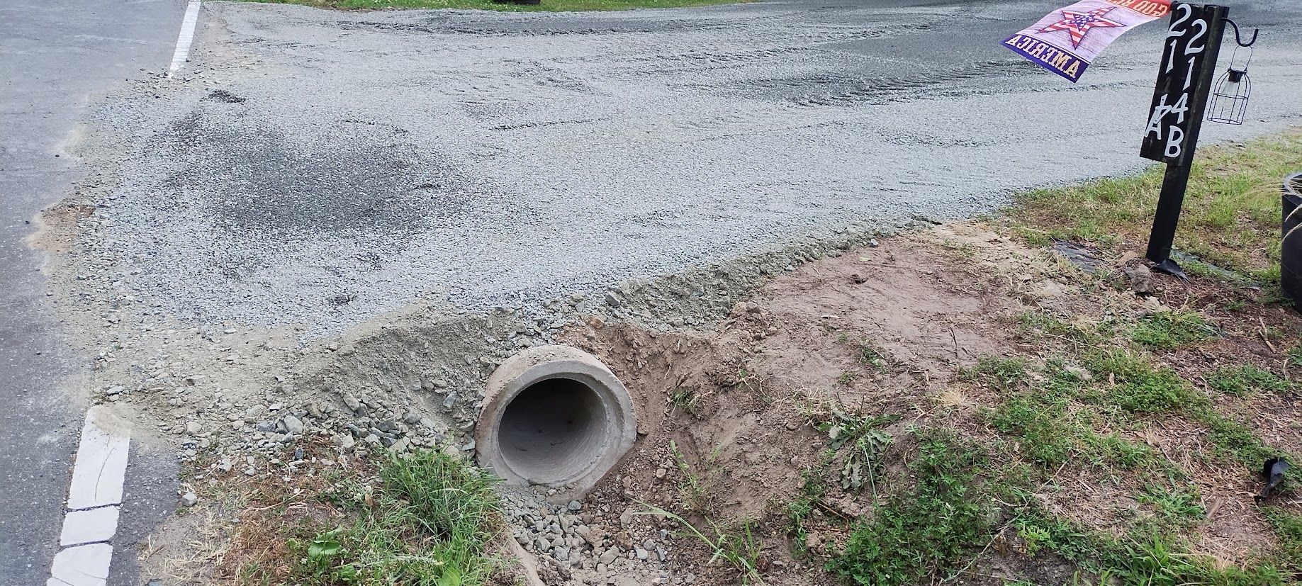 A concrete culvert pipe in a grassy area near a gravel road.