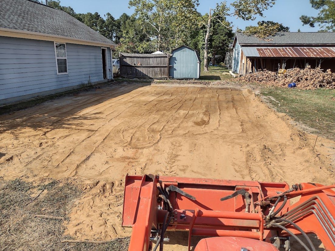 Tractor leveling a sandy area between two buildings, sunny day.