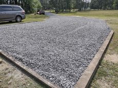Gravel pad bordered by concrete, next to a car and grassy area. A vehicle is in the background.