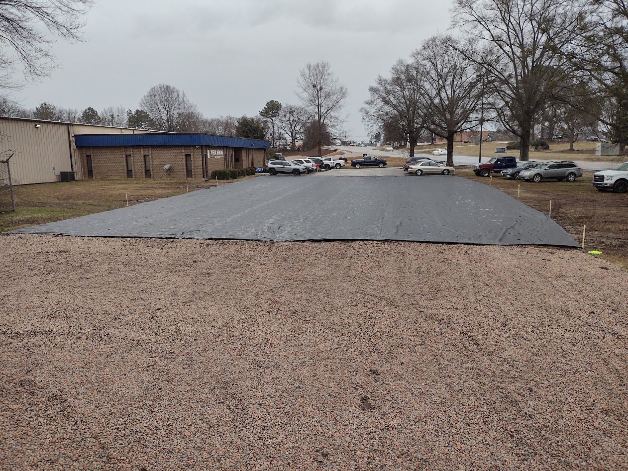 A large area of gravel with a black surface, with cars parked in the background.