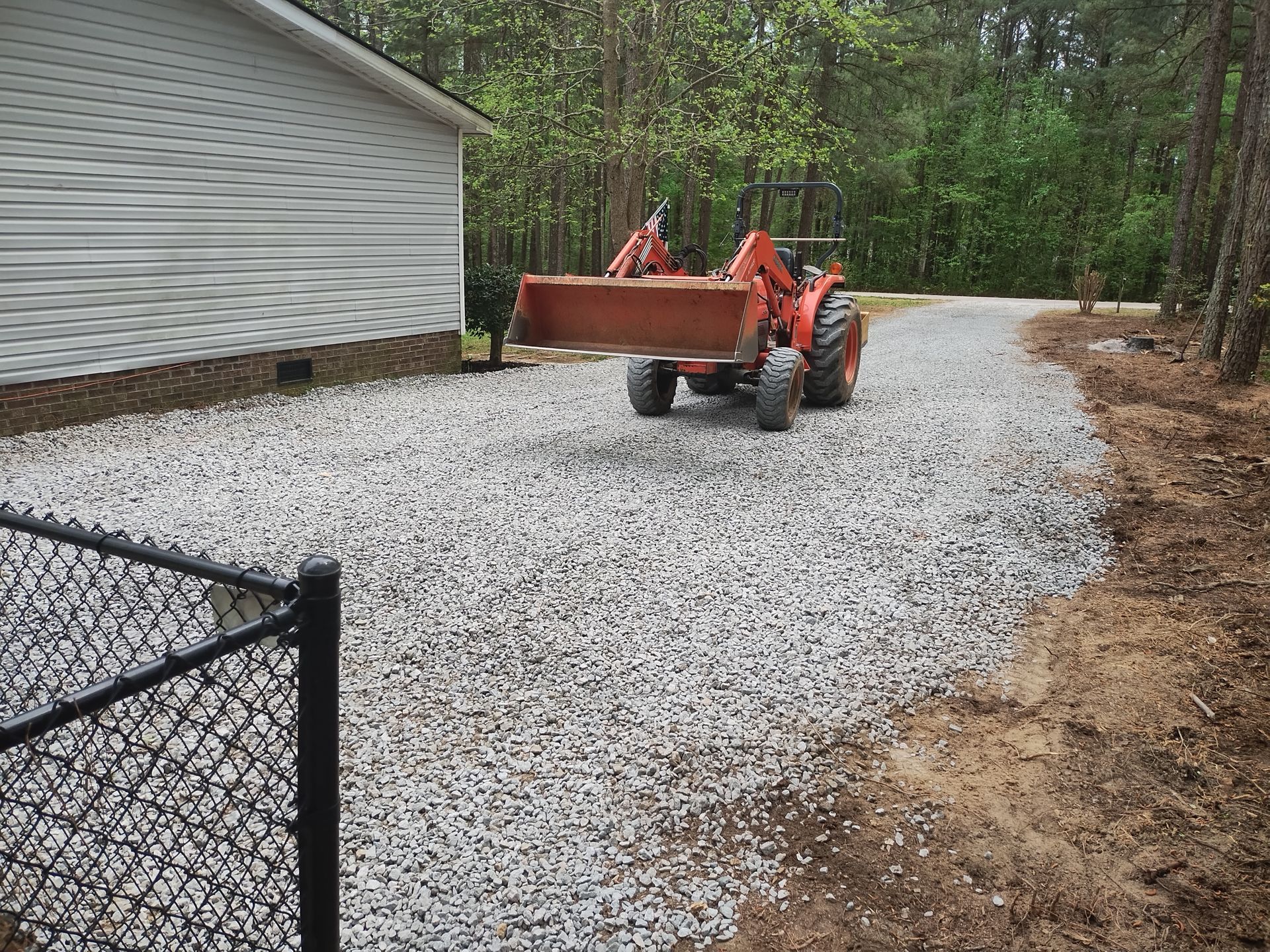 Orange tractor on gravel driveway near a house and trees.