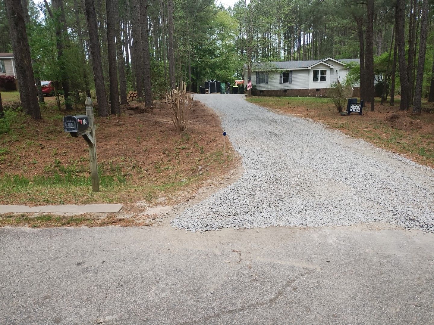 A gravel driveway curves toward a white house in a wooded setting.