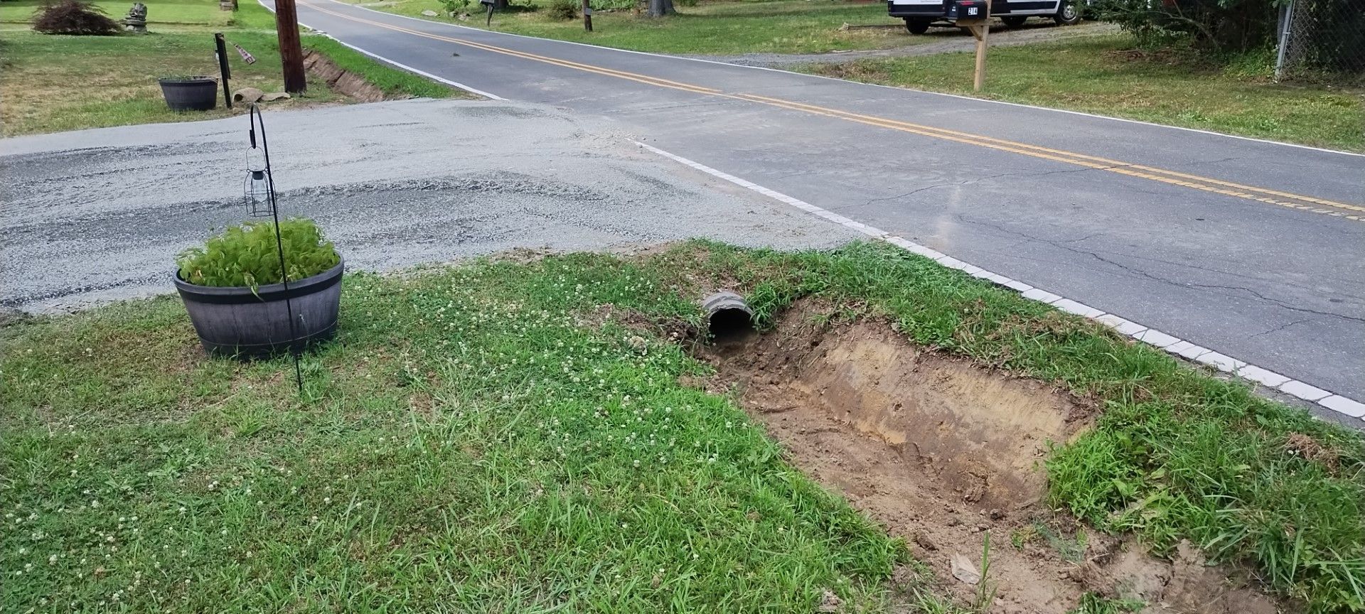 Grass, road, and culvert. A hanging basket with a plant sits on the left.