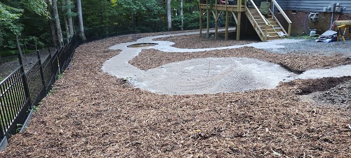 Wood chips and gravel paths in a backyard with a play structure and black fence.