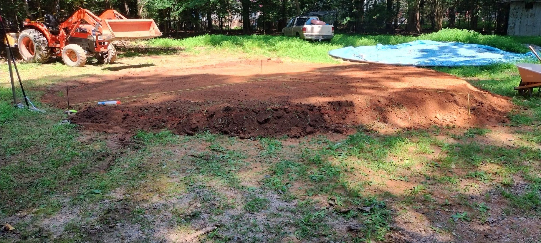 A cleared area of brown soil, likely prepared for gardening, with an orange tractor in the background.