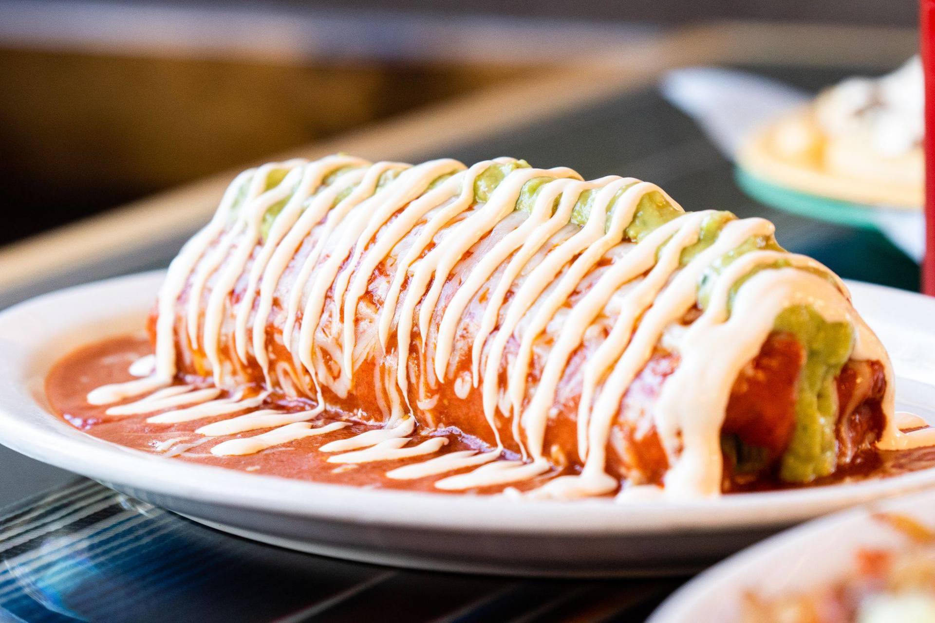 A burrito is sitting on a white plate on a table.