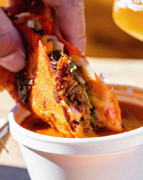 A person is dipping a burrito into a cup of sauce