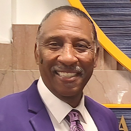 A man in a purple suit and tie is smiling for the camera.