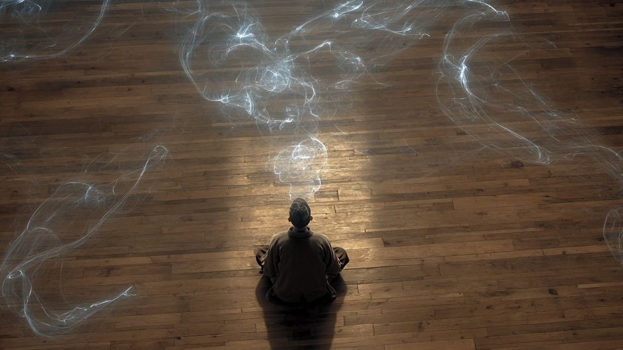 A person is sitting on a wooden floor with smoke coming out of their mouth.