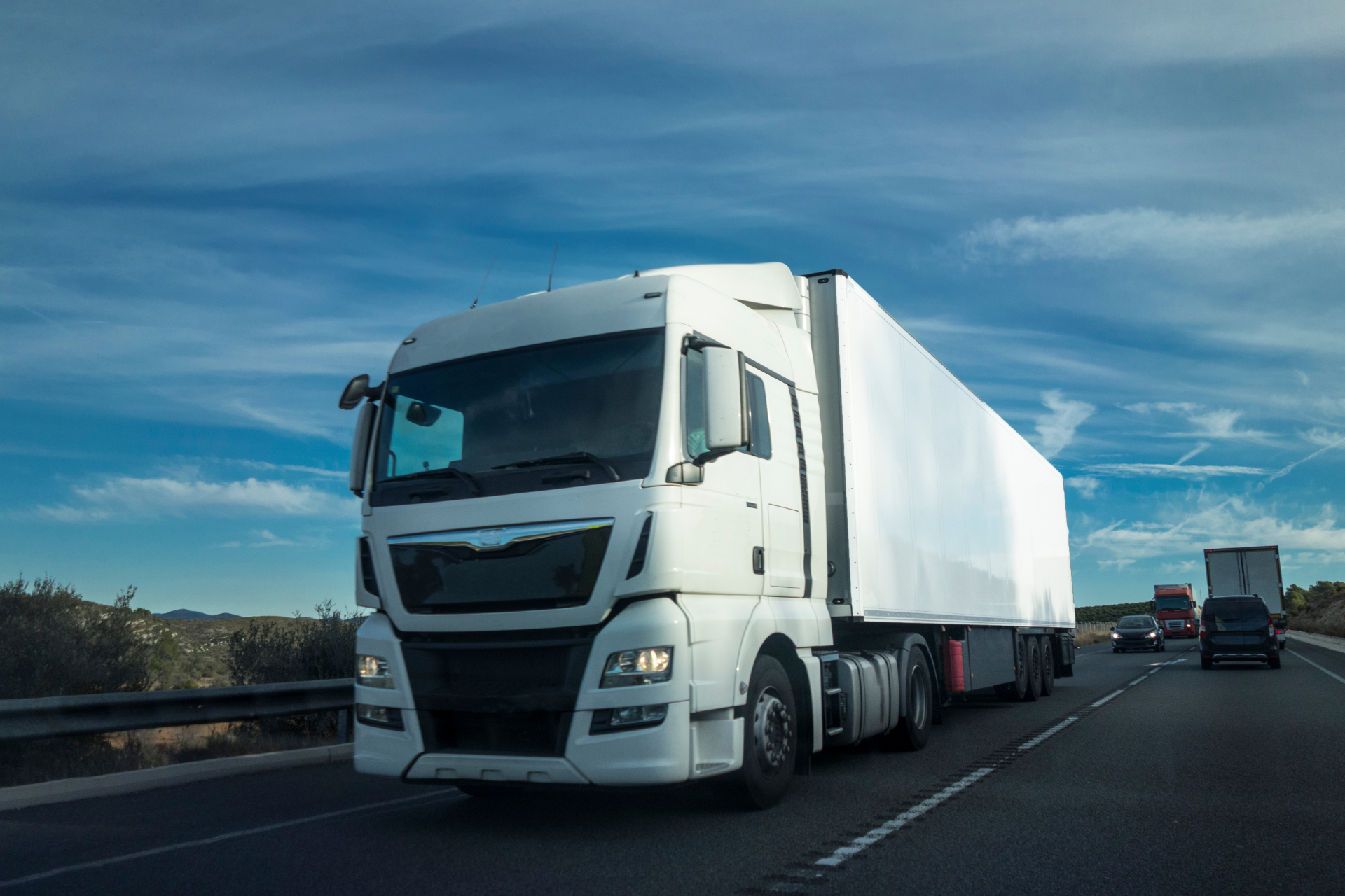 White semi-truck driving on a highway under a blue sky